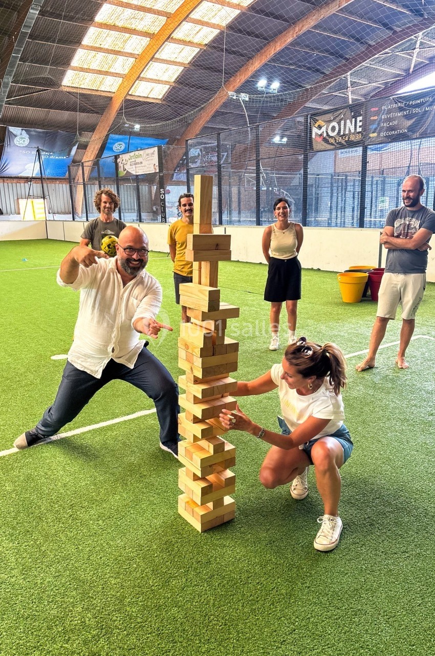 Des personnes jouent à un jeu de blocs en bois géants sur un terrain intérieur en gazon synthétique.