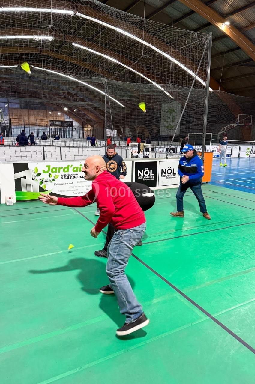 Des personnes jouent au badminton dans un gymnase, avec des terrains délimités et un filet en arrière-plan.