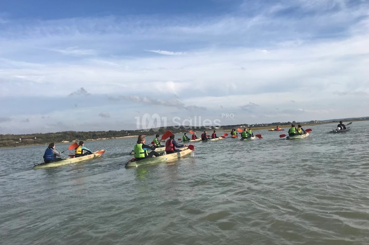 Groupe de personnes pagayant en kayak sur une étendue d'eau sous un ciel partiellement nuageux.