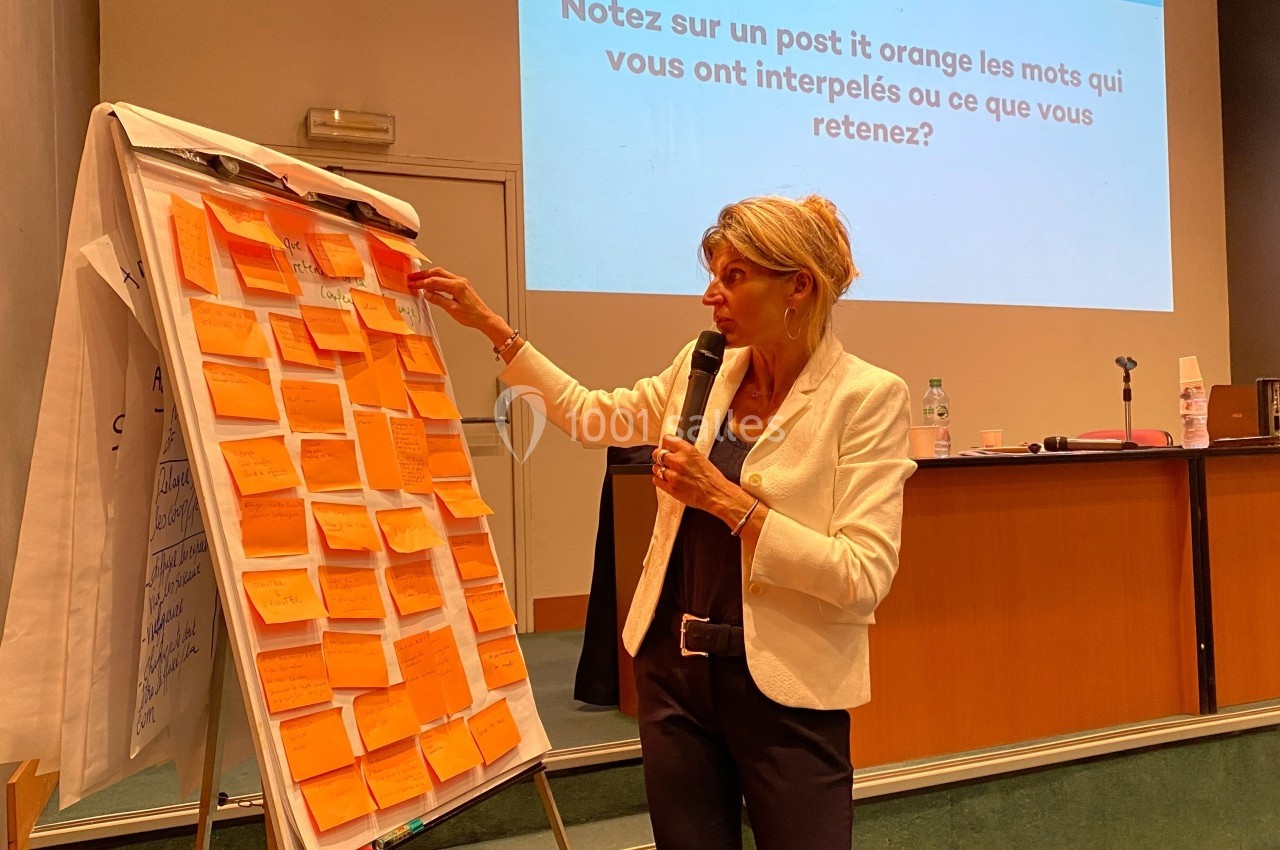 Une femme présente des idées écrites sur des post-it orange collés sur un tableau lors d'une conférence.
