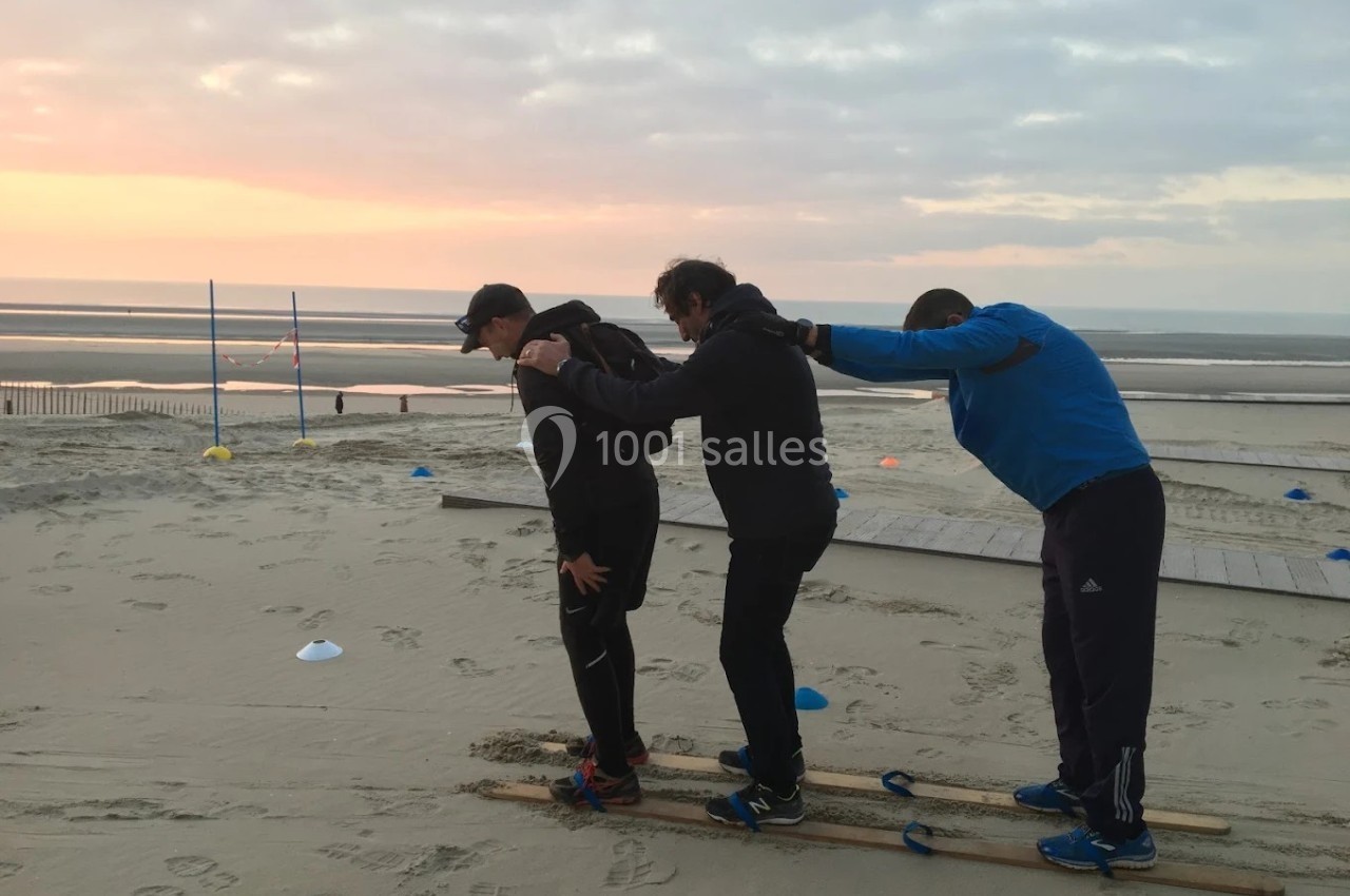 Trois personnes coopèrent sur des skis en bois sur une plage au coucher du soleil.