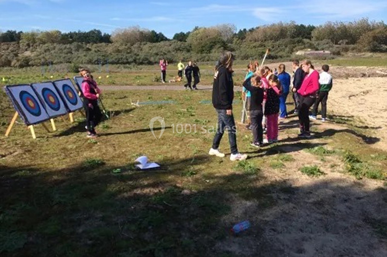 Un groupe de personnes apprend le tir à l'arc en plein air, face à des cibles installées sur un terrain dégagé.