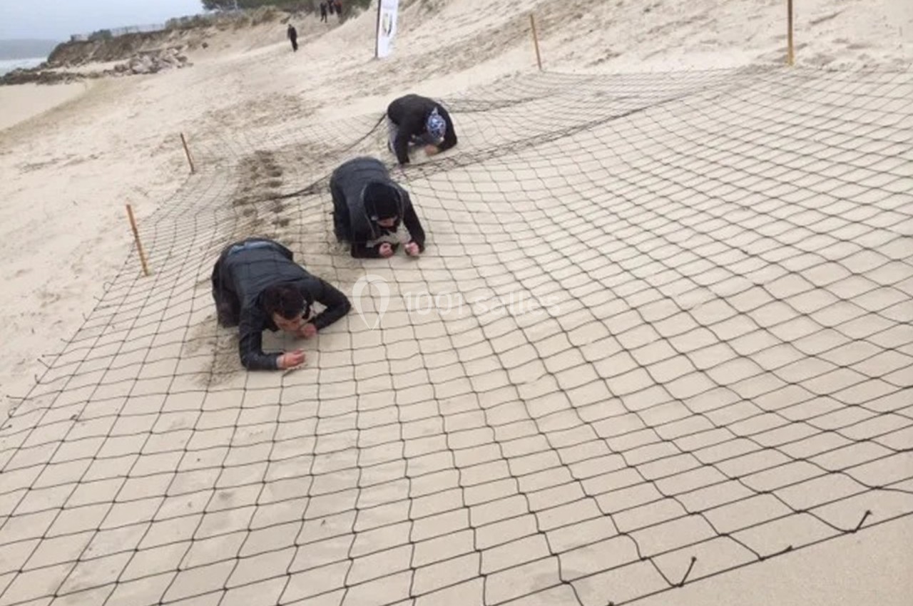 Des personnes rampent sous un filet tendu sur une plage de sable, participant à une activité ou un défi.