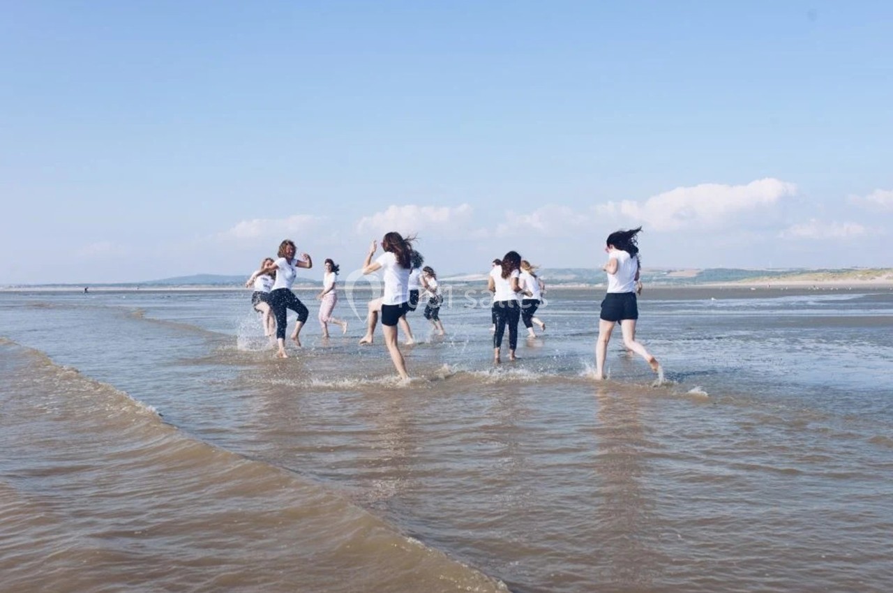 Des personnes courent et jouent dans l'eau peu profonde sur une plage sous un ciel dégagé.