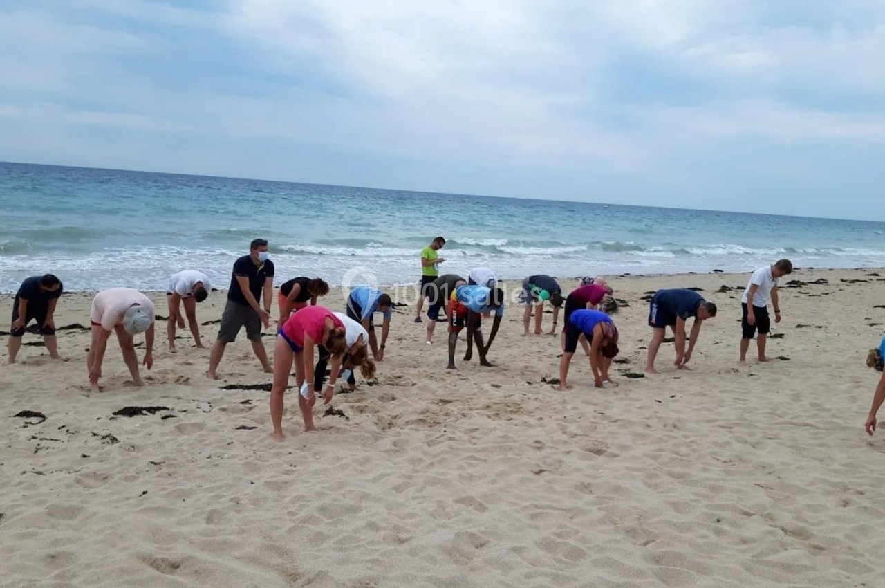Un groupe de personnes s'étire sur une plage de sable près de la mer sous un ciel nuageux.