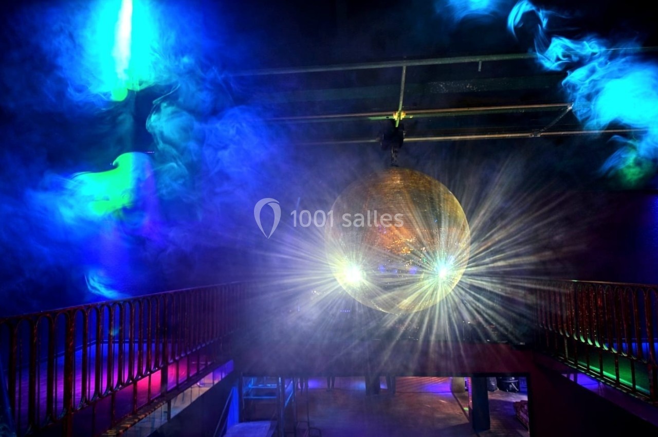 Boule disco dorée suspendue, éclairée par des projecteurs colorés, avec de la fumée créant une ambiance festive.