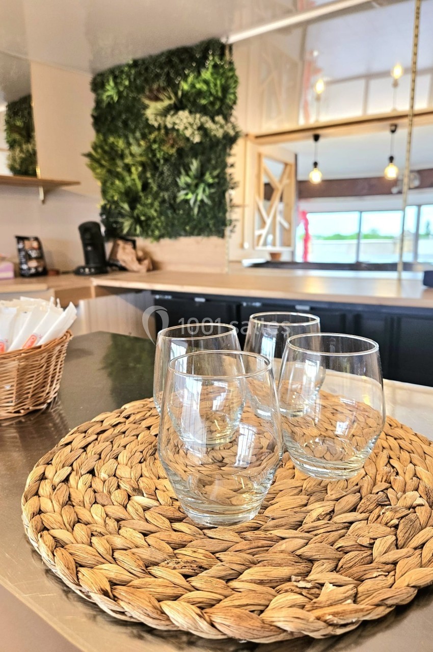 Quatre verres transparents posés sur un dessous de plat en fibres tressées dans une cuisine moderne et lumineuse.