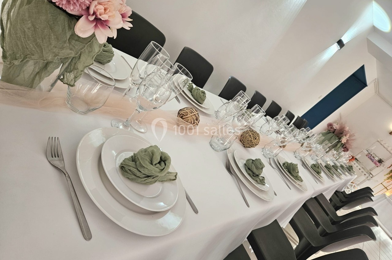 Table dressée avec une nappe blanche, vaisselle élégante, serviettes vertes et décorations florales et naturelles.