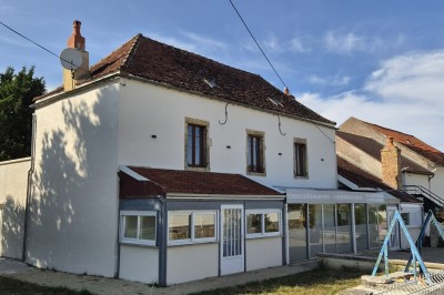 Un jardin avec pelouse, arbres et un bâtiment beige à gauche sous un ciel partiellement nuageux.