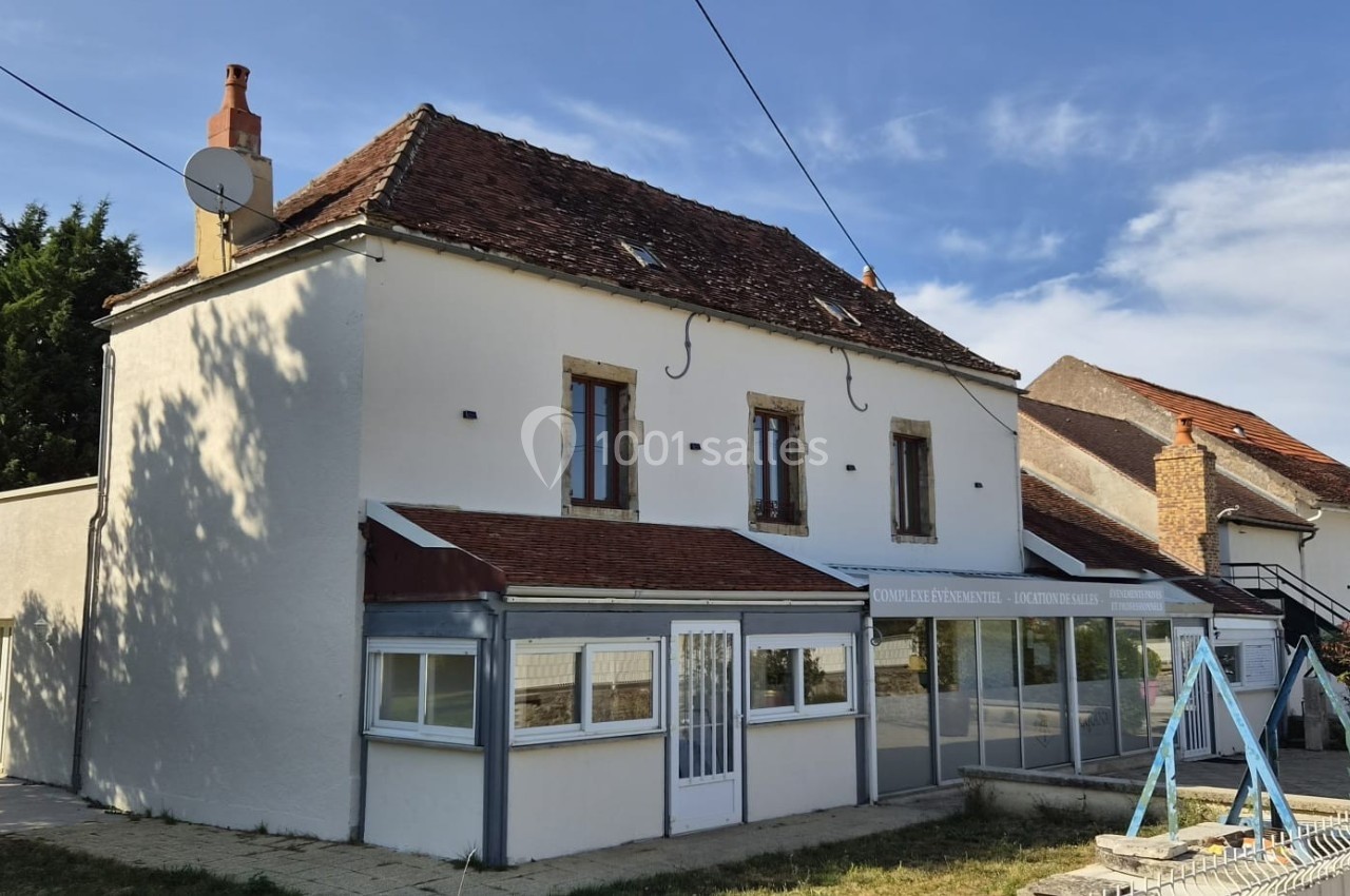 Maison traditionnelle avec façade blanche, toit en tuiles rouges, véranda et jardin sous un ciel dégagé.