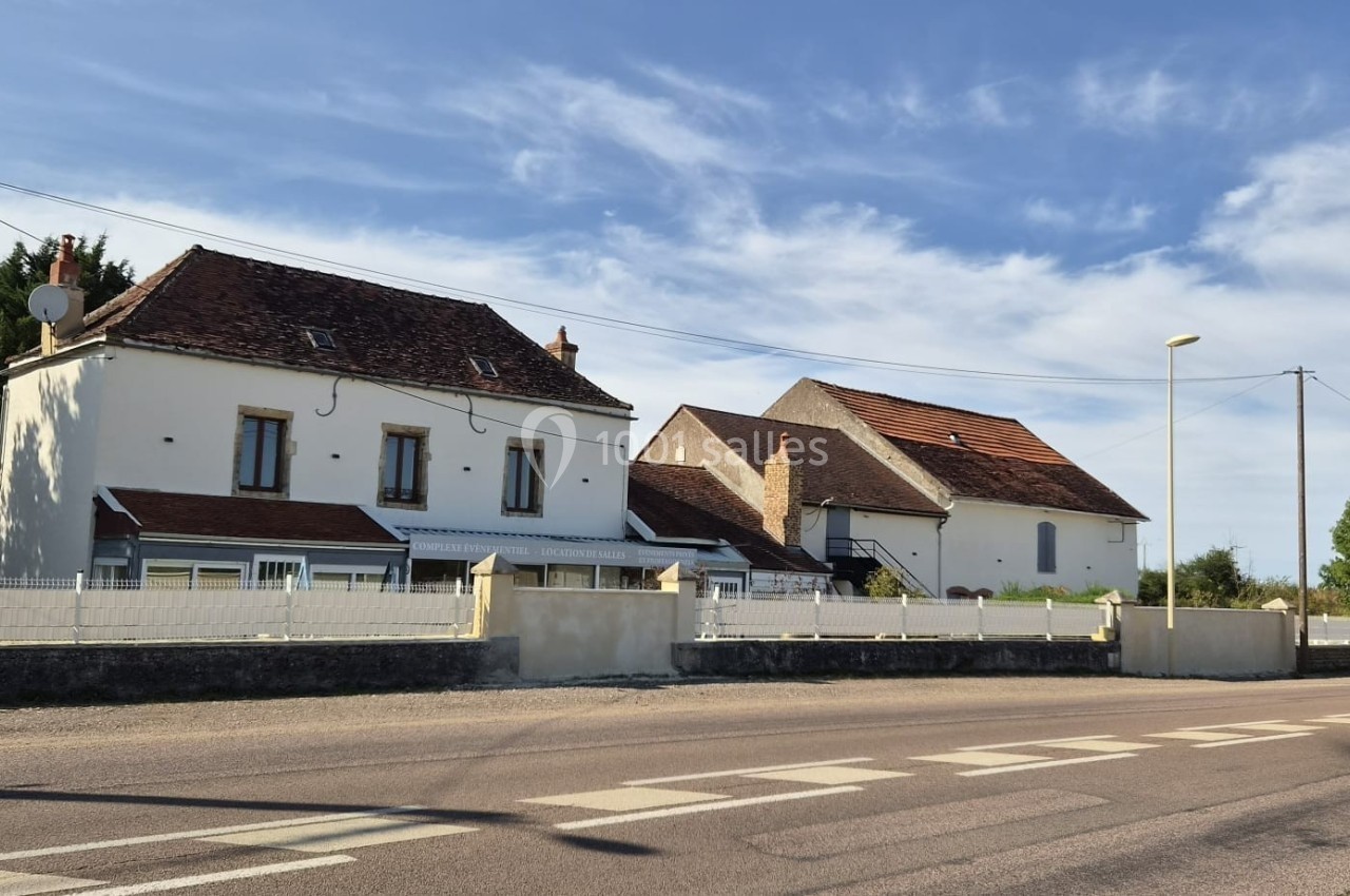 Deux maisons traditionnelles avec toits en tuiles rouges, bordées par une route et une clôture blanche, sous un ciel dégagé.