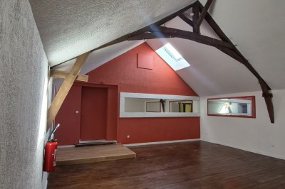 Un jardin avec pelouse, arbres et un bâtiment beige à gauche sous un ciel partiellement nuageux.