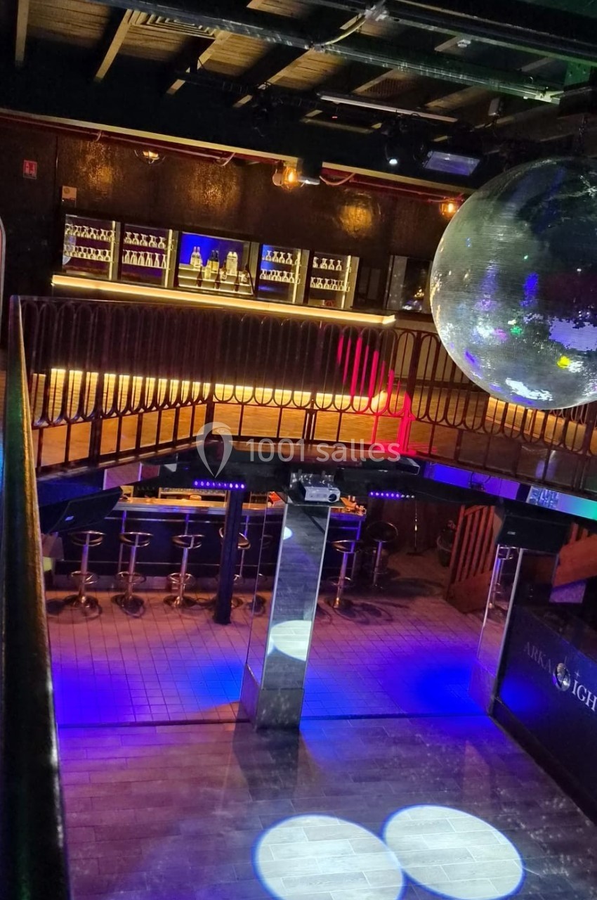 Vue intérieure d'une discothèque avec piste de danse éclairée, bar en arrière-plan et grande boule disco suspendue.