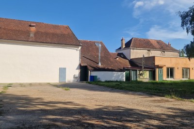Un jardin avec pelouse, arbres et un bâtiment beige à gauche sous un ciel partiellement nuageux.