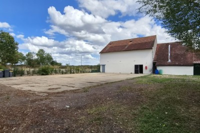 Un jardin avec pelouse, arbres et un bâtiment beige à gauche sous un ciel partiellement nuageux.