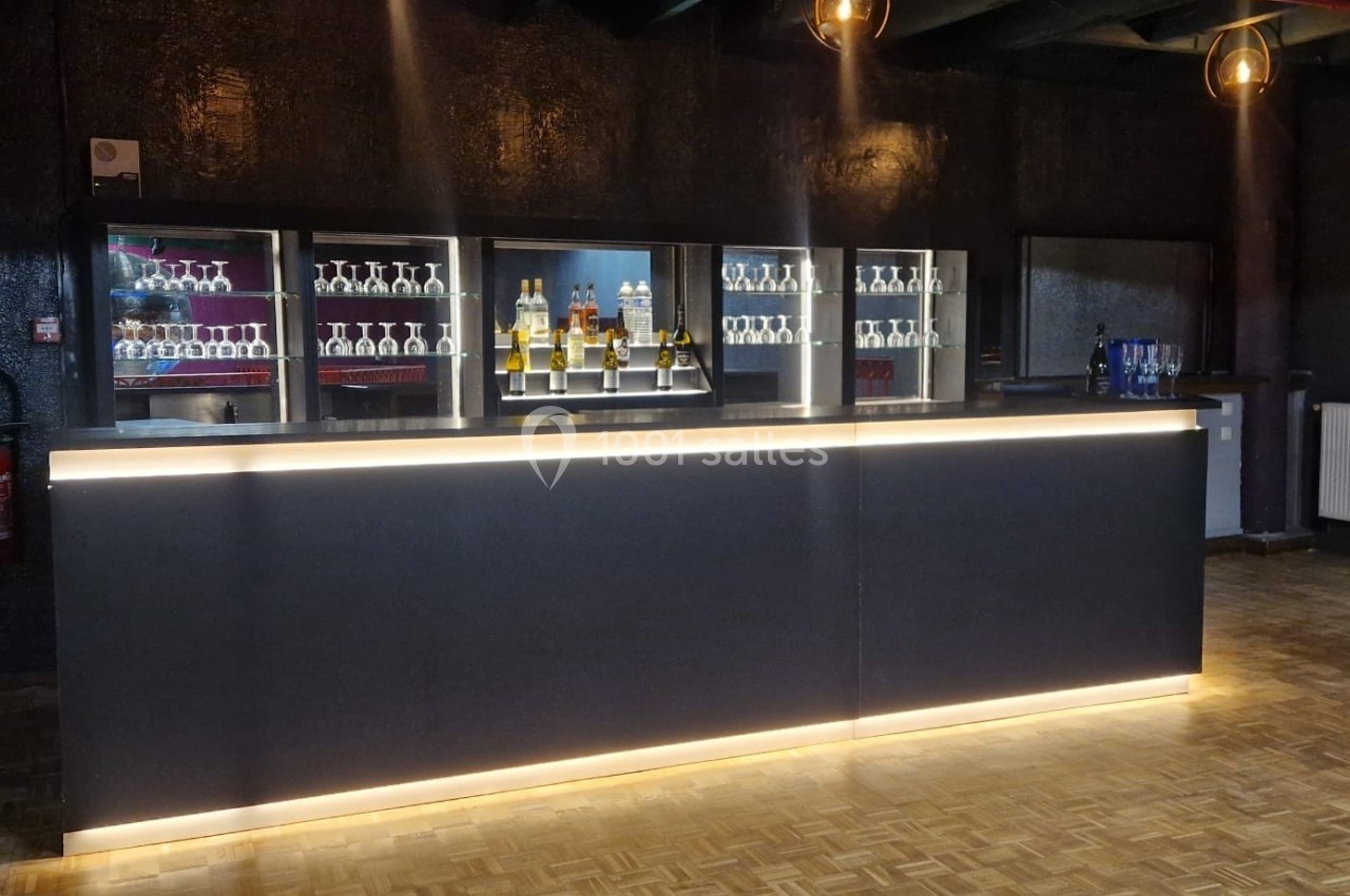 Comptoir de bar moderne éclairé, avec des étagères contenant des bouteilles et des verres en arrière-plan.