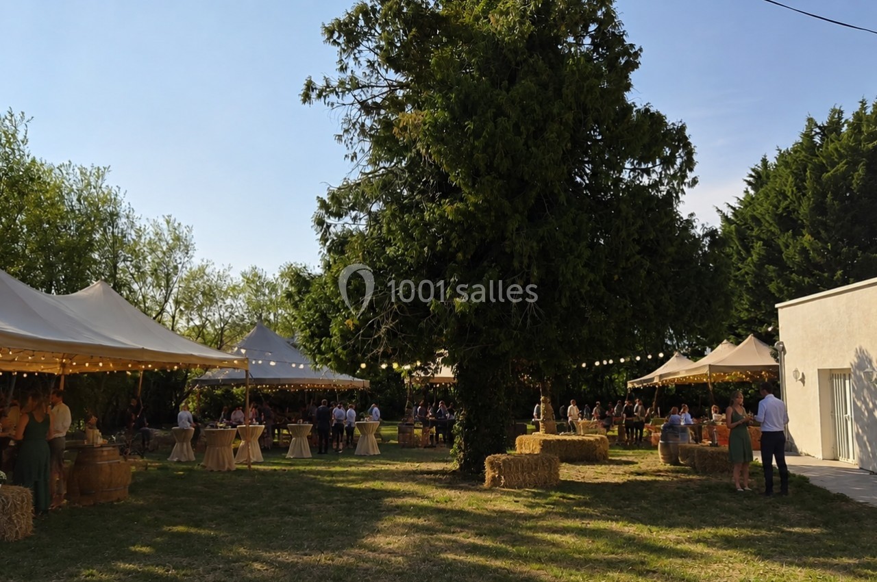 Jardin avec des tentes blanches, des tables décorées et des bottes de paille, lors d'un événement en plein air.