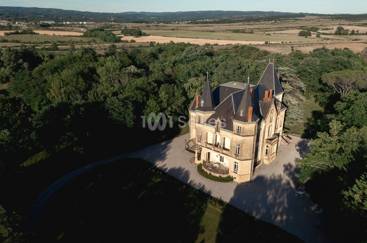Château de pierre avec tourelles à toits pointus, entouré de verdure et surplombant une vallée agricole.