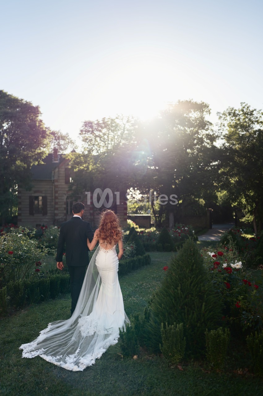 Couple marié dans un jardin planté de rosiers rouges face à un château en pierre au coucher de soleil.