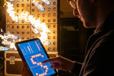 Un homme de dos observe un mur de dispositifs avec des flammes jaillissant à l'extérieur, entouré de végétation.