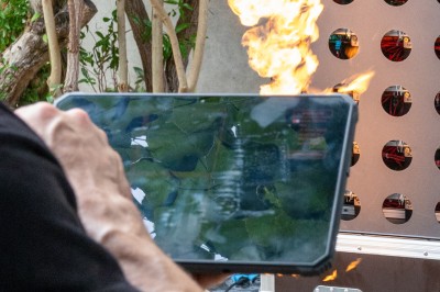 Un homme de dos observe un mur de dispositifs avec des flammes jaillissant à l'extérieur, entouré de végétation.