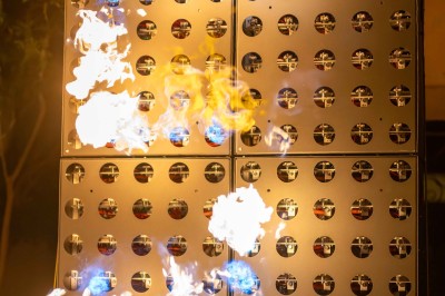 Miniature Rêves de Feu #6 Colonnes de panneaux métalliques perforés émettant des flammes dans un environnement extérieur nocturne.