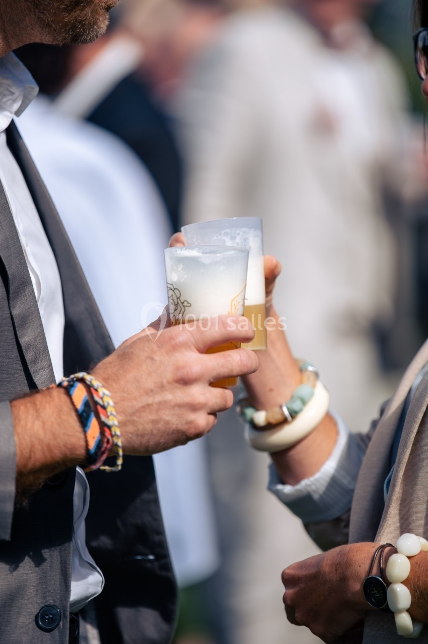 Deux personnes trinquent avec des verres de bière en plastique lors d'un événement en extérieur.