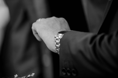 Main d'une personne en costume portant une montre-bracelet métallique, cadrée en noir et blanc.