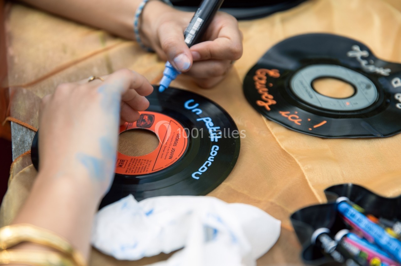 Personne écrivant au marqueur bleu sur un disque vinyle posé sur une table avec des crayons et des tissus.