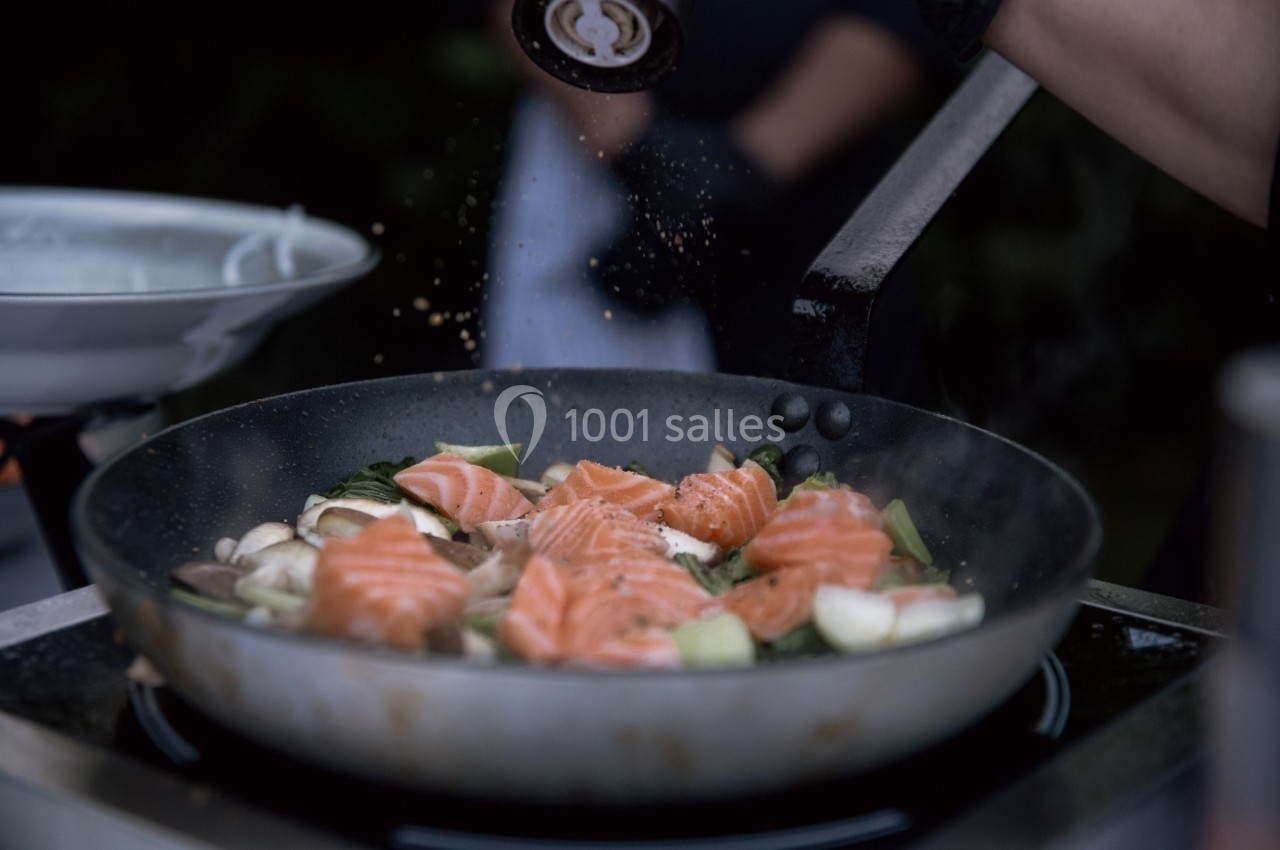 Filets de saumon frais cuisant dans une poêle avec des légumes, saupoudrés d'assaisonnement.