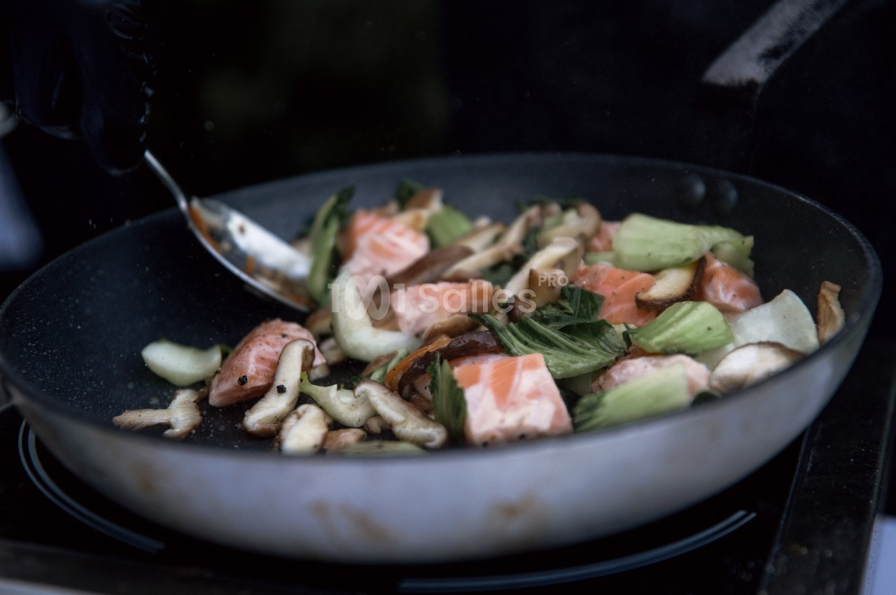 Légumes sautés et morceaux de saumon cuits dans une poêle, remués avec une cuillère en métal.