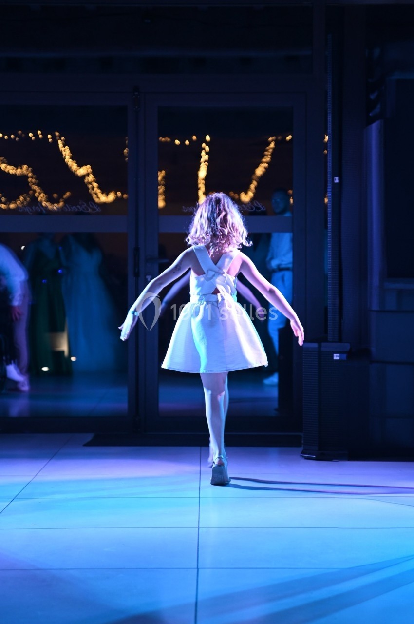 Une jeune fille en robe blanche danse sous des lumières tamisées dans un espace intérieur.