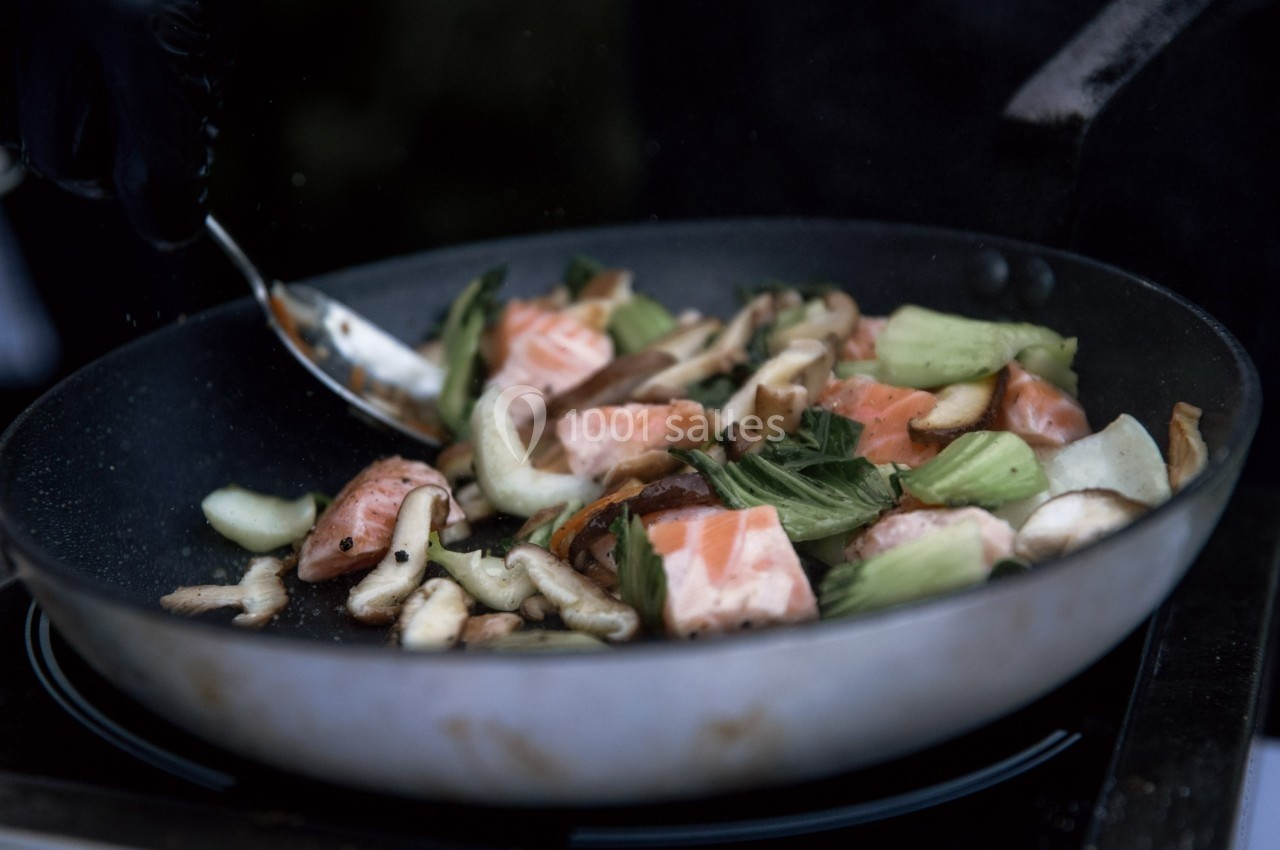 Légumes sautés et morceaux de saumon cuits dans une poêle, remués avec une cuillère en métal.