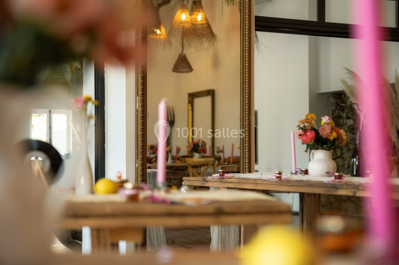 Salle décorée avec des fleurs colorées, des bougies roses et des tables en bois, reflétée dans un grand miroir.