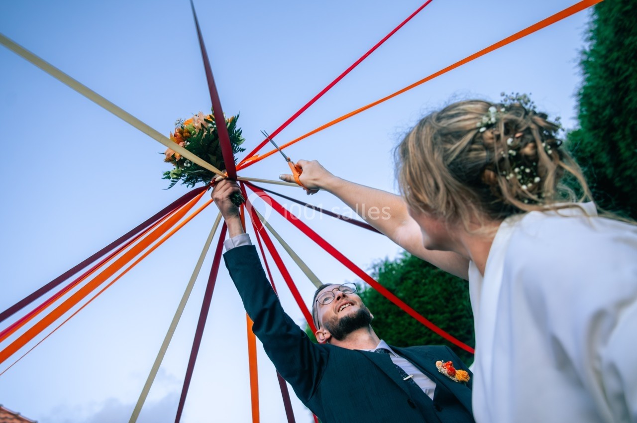 Un couple tient des rubans colorés attachés à un bouquet de fleurs lors d'une célébration en plein air.