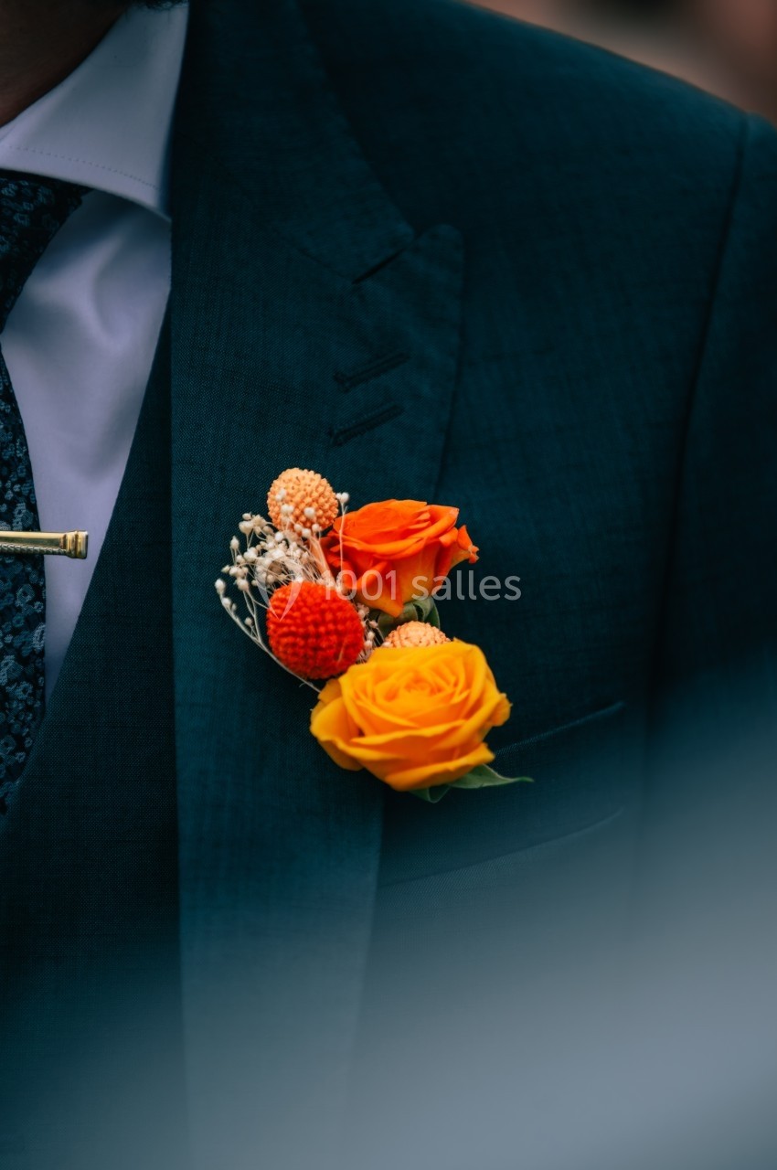 Boutonnière composée de fleurs orange et jaunes portée sur un costume sombre avec une cravate à motifs.