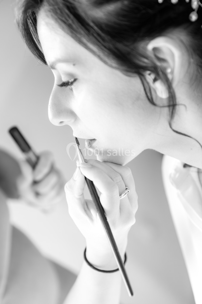Femme de profil se faisant maquiller les lèvres avec un pinceau dans un cadre lumineux.