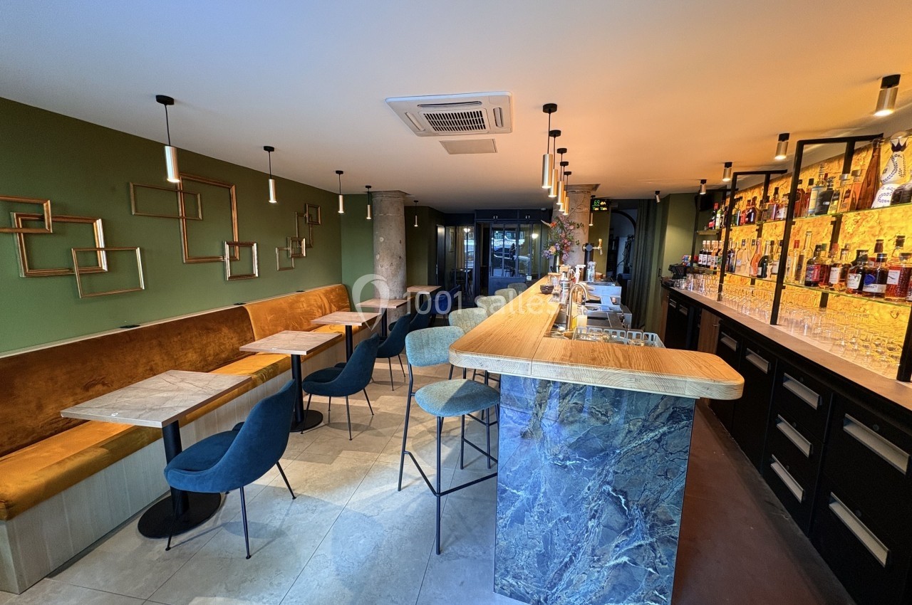 Intérieur d'un bar moderne avec comptoir en marbre, rangée de bouteilles, tables et chaises dans un décor chaleureux.