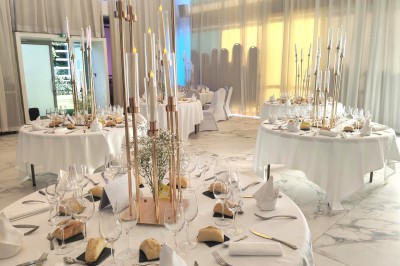 Salle de réception élégante décorée de fleurs blanches, chandeliers dorés et éclairages roses.