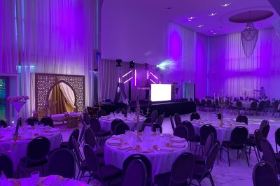 Salle de réception élégante décorée de fleurs blanches, chandeliers dorés et éclairages roses.