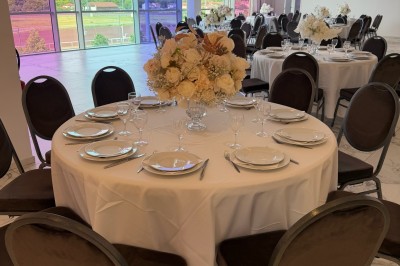 Salle extérieure aménagée avec des tables hautes noires, décorations florales blanches et lumière naturelle.