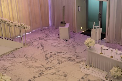 Salle extérieure aménagée avec des tables hautes noires, décorations florales blanches et lumière naturelle.