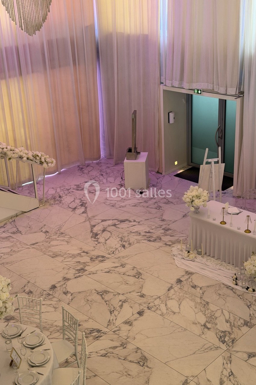 Salle de réception avec sol en marbre, rideaux translucides, tables décorées et une table de buffet près d'une porte ouverte.