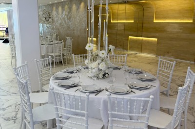 Salle extérieure aménagée avec des tables hautes noires, décorations florales blanches et lumière naturelle.