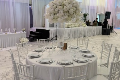 Salle extérieure aménagée avec des tables hautes noires, décorations florales blanches et lumière naturelle.