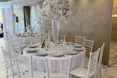 Salle extérieure aménagée avec des tables hautes noires, décorations florales blanches et lumière naturelle.