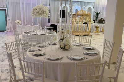 Salle extérieure aménagée avec des tables hautes noires, décorations florales blanches et lumière naturelle.
