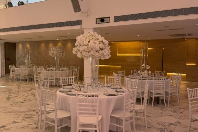 Salle extérieure aménagée avec des tables hautes noires, décorations florales blanches et lumière naturelle.