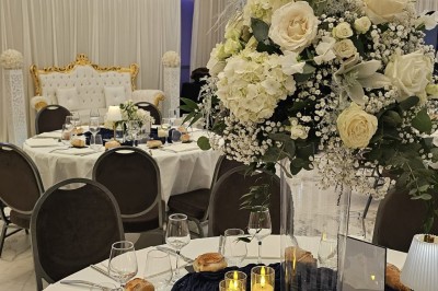 Salle extérieure aménagée avec des tables hautes noires, décorations florales blanches et lumière naturelle.