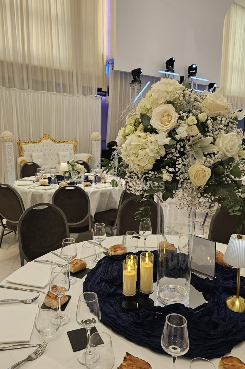 Salle de réception élégante avec tables dressées, centre de table floral, chandelles et décorations raffinées.